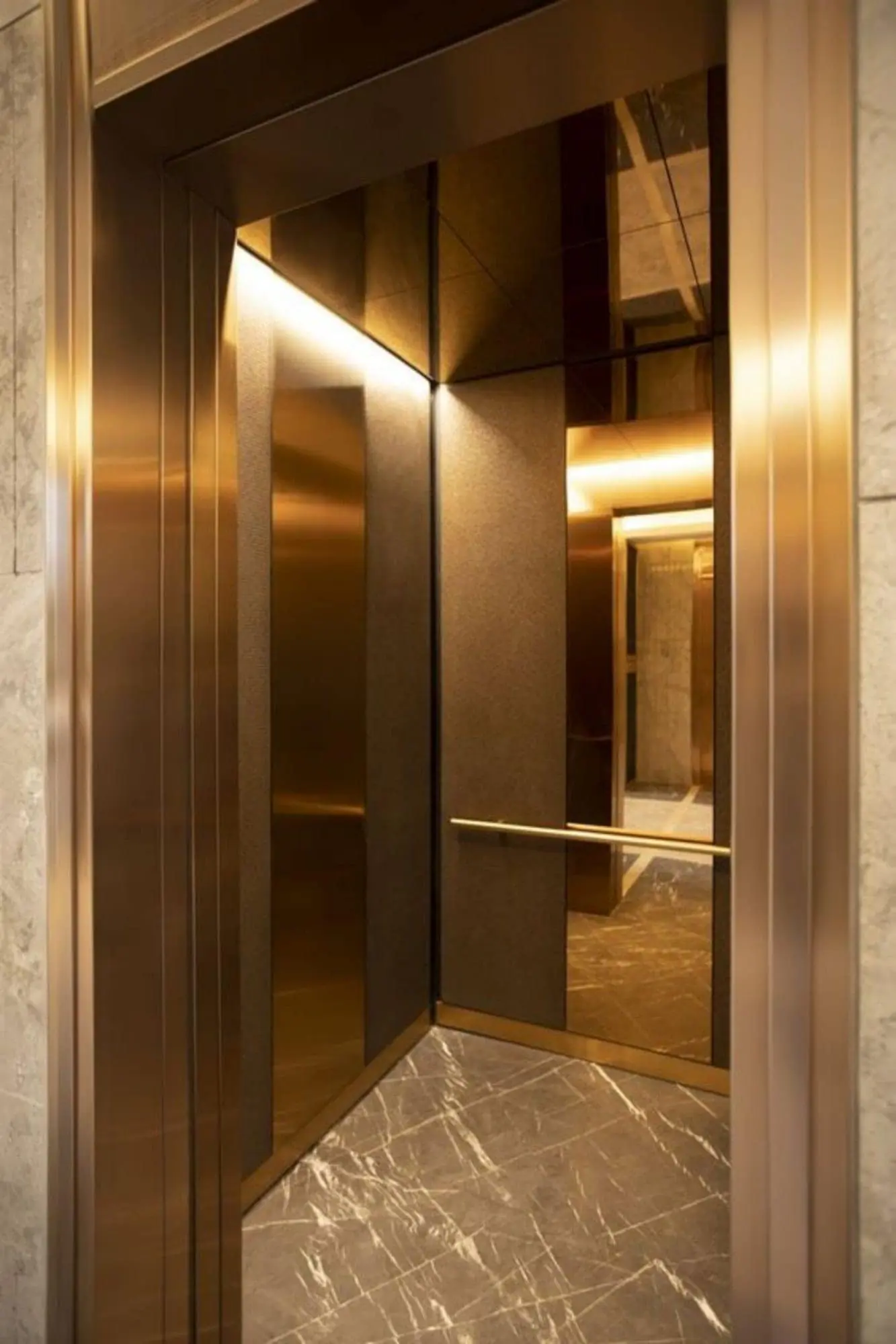 A bronze finish CASTOR cabin interior with mirrored wall panels, its doors open onto a dark marble landing.