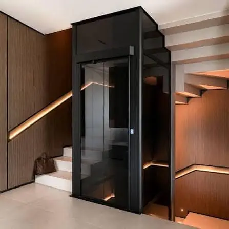 Black framed glass ESTELLA shaft installed beside a wood panelled staircase with warm LED strip lighting under the treads.
